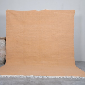 May include: A large, rectangular, solid orange rug with a white fringe border. The rug is laying flat on a gray concrete floor.