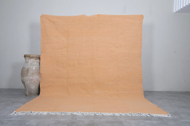 May include: A large, rectangular, solid orange rug with a white fringe border. The rug is laying flat on a gray concrete floor.