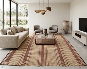 Op de afbeelding: Een moderne woonkamer met een beige bank, twee grijze fauteuils en een rechthoekige salontafel. Een groot, rechthoekig tapijt met bruine en beige strepen bedekt de vloer. Een grote tv is gemonteerd op een lage, lichtgrijze kast.