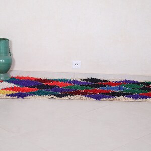 May include: A colorful, hand-woven rug with a geometric pattern in shades of red, blue, green, yellow, and white. The rug is laid out on a white tiled floor.