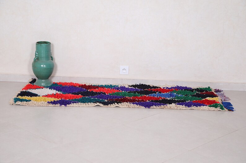 May include: A colorful, hand-woven rug with a geometric pattern in shades of red, blue, green, yellow, and white. The rug is laid out on a white tiled floor.