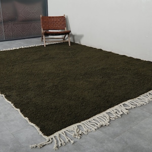 May include: A dark green shag rug with a white fringe border. The rug is laid out on a gray floor.