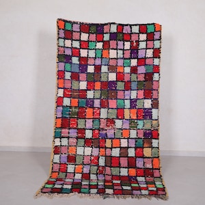 May include: A colorful Moroccan rug with a geometric pattern of squares in various shades of red, green, blue, purple, and orange. The rug has a fringe border and is made of wool.