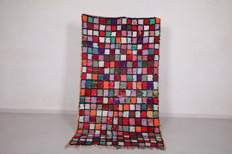 May include: A colorful Moroccan rug with a geometric pattern of squares in various shades of red, green, blue, purple, and orange. The rug has a fringe border and is made of wool.