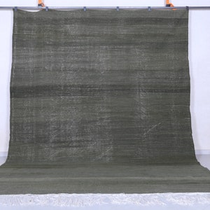 May include: A dark green rug with a subtle pattern and white fringe. The rug is hanging on a wall.