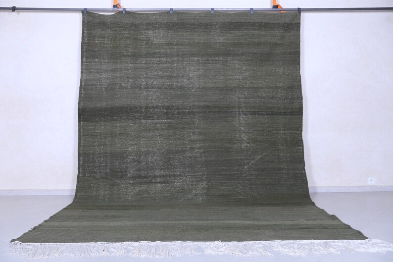 May include: A dark green rug with a subtle pattern and white fringe. The rug is hanging on a wall.