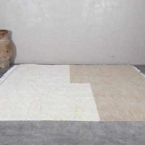 Puede incluir: Una alfombra tejida a mano de color blanco y beige con un dise&ntilde;o geom&eacute;trico. La alfombra tiene un borde de flecos.