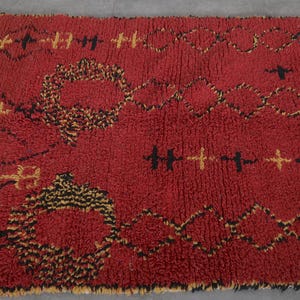 May include: A red Moroccan rug with a geometric pattern in black and yellow. The rug has a thick, fluffy texture.