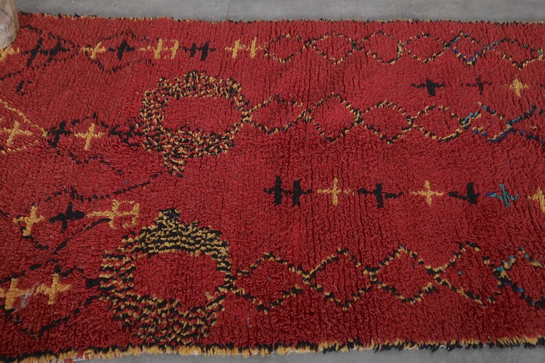 May include: A red Moroccan rug with a geometric pattern in black and yellow. The rug has a thick, fluffy texture.