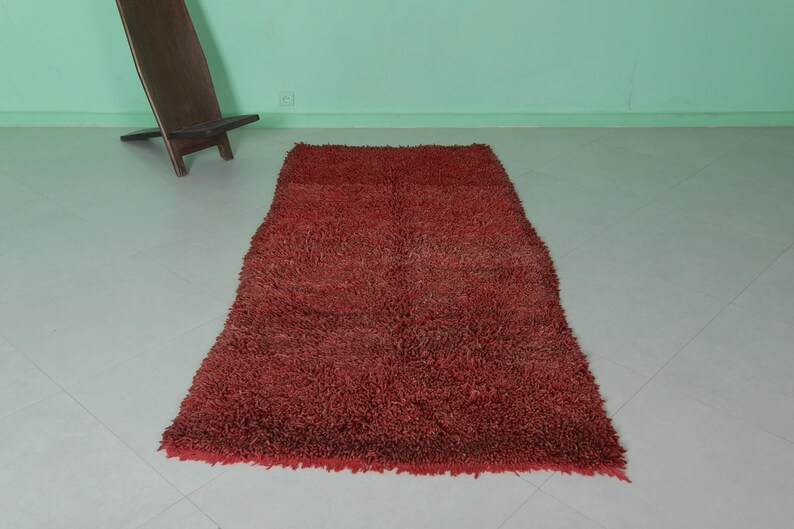 May include: A red shag rug with a long, rectangular shape. The rug has a soft, fluffy texture and is perfect for adding a touch of warmth and comfort to any room.