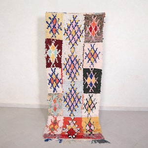May include: A colorful Moroccan rug with a geometric pattern in shades of red, blue, yellow, and white. The rug is made of wool and has a fringe on the ends.