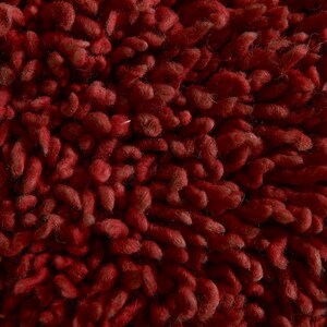 May include: Close-up of a deep red, textured rug with a fuzzy, looped pile.
