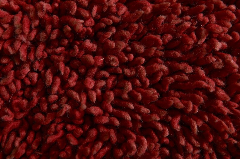 May include: Close-up of a deep red, textured rug with a fuzzy, looped pile.