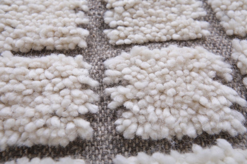May include: Close-up of a white, fluffy rug with a textured, woven pattern. The rug has a raised, tufted design, creating a soft and inviting look.