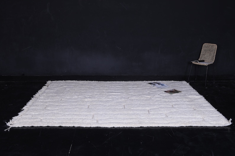 May include: White shag rug with a textured brick pattern. The rug has a fringe border and is laid out on a black floor.