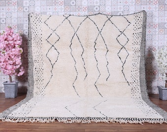 May include: A white Moroccan rug with a black diamond pattern. The rug has a fringe border and is made of wool.