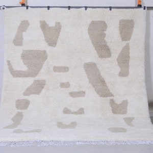 May include: A white and beige shag rug with an abstract pattern. The rug has a fringe border.