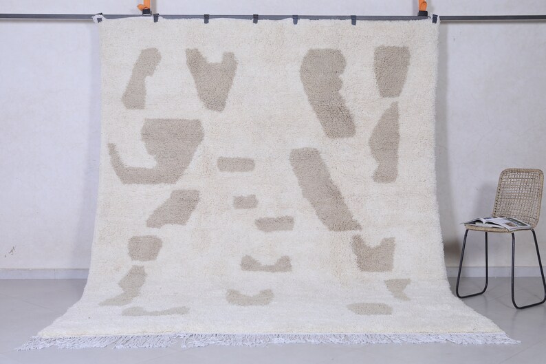 May include: A white and beige shag rug with an abstract pattern. The rug has a fringe border.