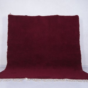 May include: A deep burgundy shag rug with a white fringe border. The rug is folded in half and lying on a white surface.