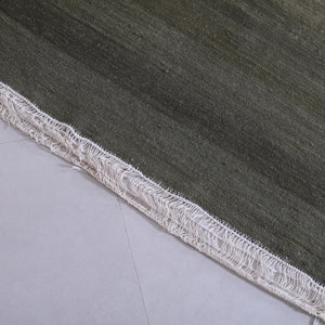 May include: Close-up of a green rug with a white fringe border. The rug has a subtle striped pattern.