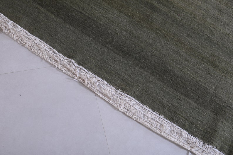 May include: Close-up of a green rug with a white fringe border. The rug has a subtle striped pattern.