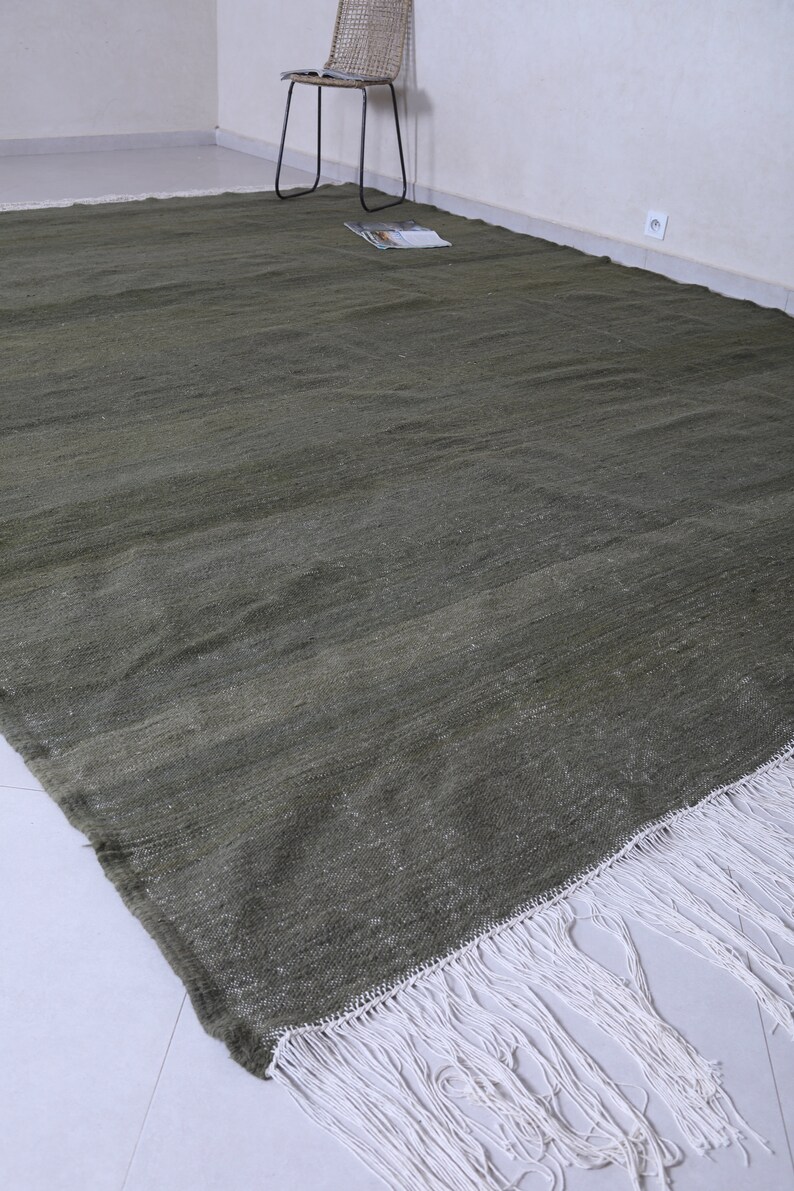 May include: A green rug with a white fringe. The rug is made of a soft, woven material and has a subtle texture.