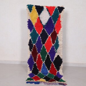 May include: A colorful Moroccan rug with a geometric diamond pattern in shades of red, blue, green, yellow, and white. The rug has a fringe border and is made of wool.