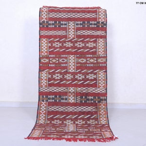 May include: A red, white, and black patterned runner rug with geometric designs. The rug is 77 cm by 174 cm, or 2.5 feet by 5.7 feet.