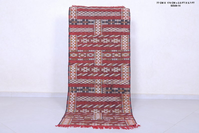 May include: A red, white, and black patterned runner rug with geometric designs. The rug is 77 cm by 174 cm, or 2.5 feet by 5.7 feet.