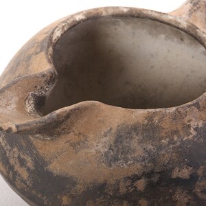May include: A brown clay pot with a wide opening and a handle. The pot has a rough, textured surface and appears to be very old.