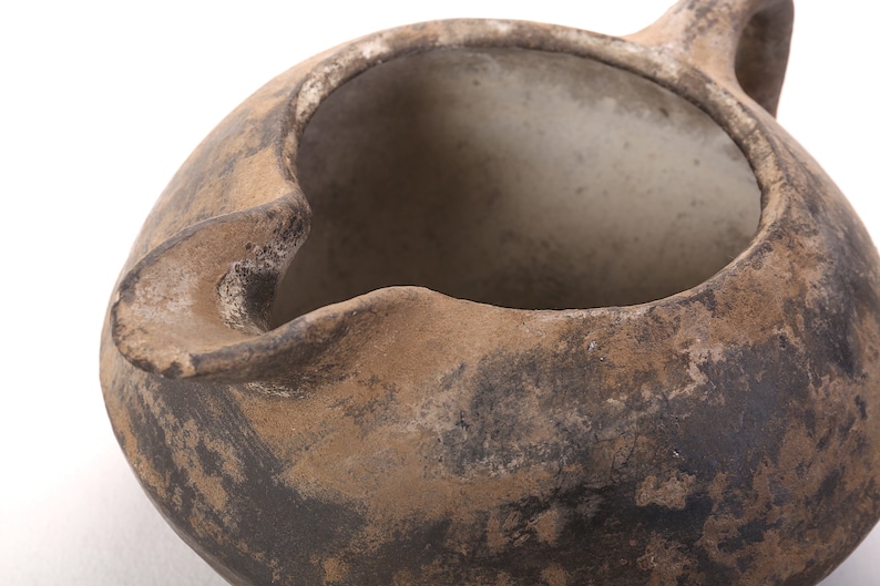 May include: A brown clay pot with a wide opening and a handle. The pot has a rough, textured surface and appears to be very old.