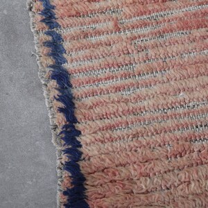 May include: Close-up of a pink and white woven rug with a blue fringe border.