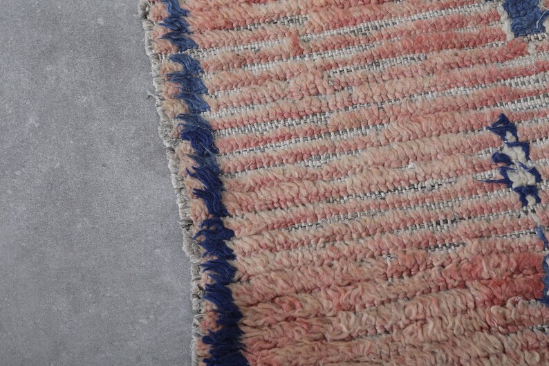 May include: Close-up of a pink and white woven rug with a blue fringe border.