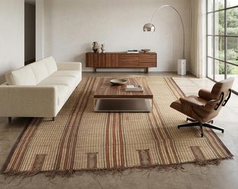 May include: A modern living room featuring a cream-colored sofa, a wooden coffee table, and a leather armchair. A large, rectangular rug with vertical stripes in shades of brown and beige covers the floor. A wooden cabinet and a floor lamp complete the scene.