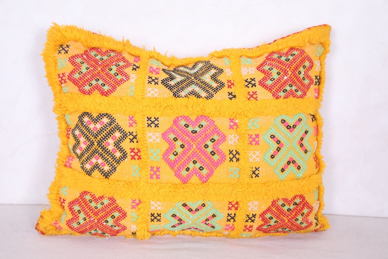 K&ouml;nnte beinhalten: Gelbes Kissen mit geometrischem Muster in Rot-, Rosa-, Gr&uuml;n- und Schwarzt&ouml;nen. Das Kissen hat einen Fransenrand.