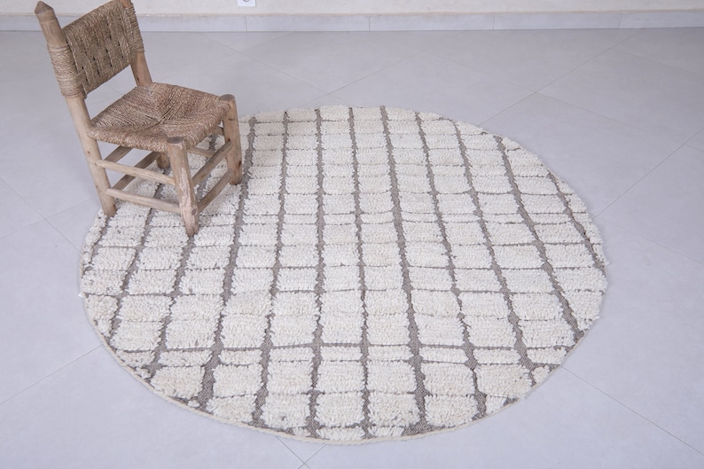 May include: A round, white and gray woven rug with a geometric pattern. The rug is on a tiled floor and a small wooden chair is sitting on the rug.