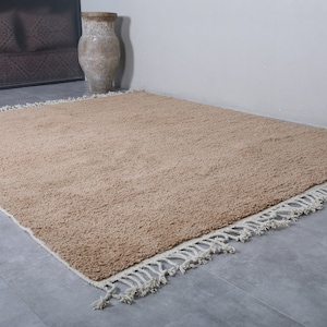 May include: A light brown shag rug with a white fringe border. The rug is laid out on a gray tiled floor.