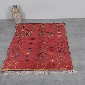 May include: A red Moroccan rug with a geometric pattern in yellow, blue, and black. The rug has a fringe border.