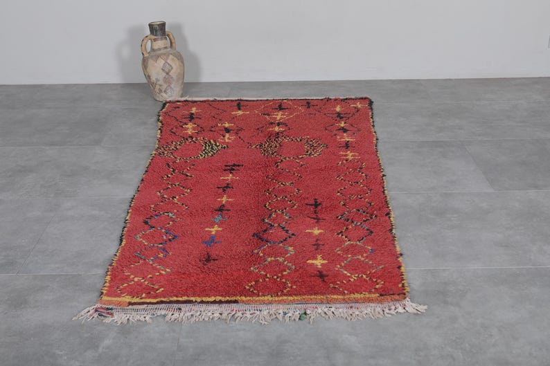 May include: A red Moroccan rug with a geometric pattern in yellow, blue, and black. The rug has a fringe border.