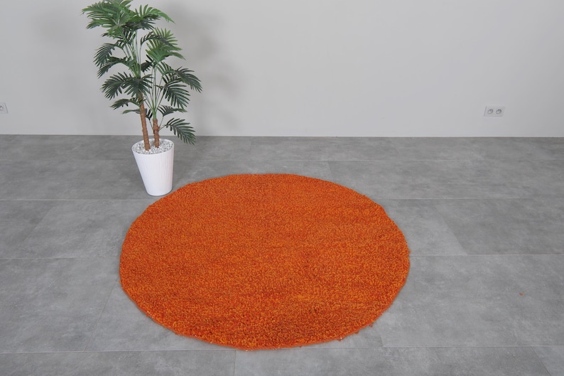 May include: A round, orange shag rug on a gray tiled floor.