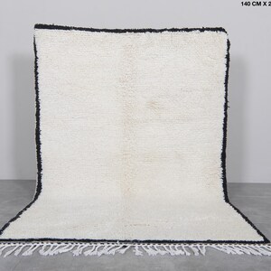 Op de afbeelding: Witte shaggy vloerkleed met een zwarte rand en franjes. Het vloerkleed is 1,40 meter bij 2 meter.
