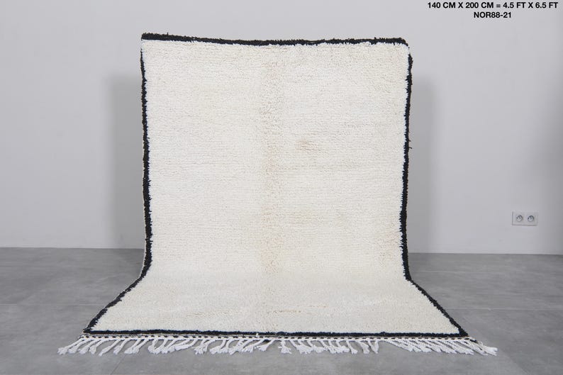 Op de afbeelding: Witte shaggy vloerkleed met een zwarte rand en franjes. Het vloerkleed is 1,40 meter bij 2 meter.
