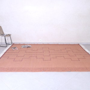 May include: A light brown woven rug with a geometric pattern and white fringe. The rug is laid out on a white tiled floor.