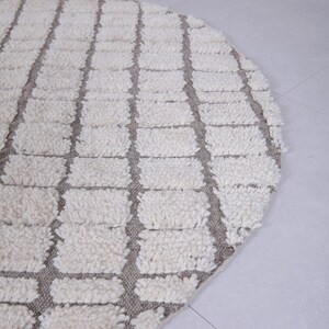 May include: A round, white and gray rug with a geometric pattern. The rug is made of a soft, fluffy material.