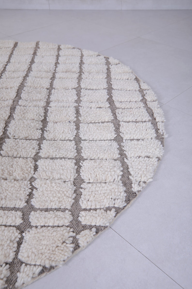 May include: A round, white and gray rug with a geometric pattern. The rug is made of a soft, fluffy material.
