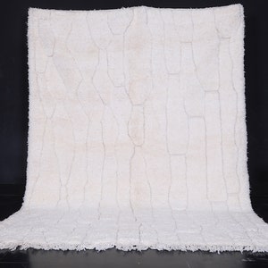 May include: A white shag rug with a geometric pattern. The rug has a fringe border and is laid out on a black surface.