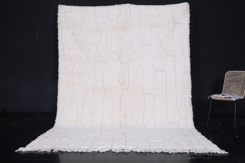 May include: A white shag rug with a geometric pattern. The rug has a fringe border and is laid out on a black surface.