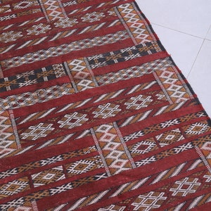 May include: A red, brown, and white patterned rug with geometric designs. The rug has a fringe on the top edge.