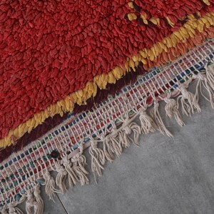 May include: A red, yellow, and white Moroccan rug with a fringe border. The rug has a textured, fluffy surface.
