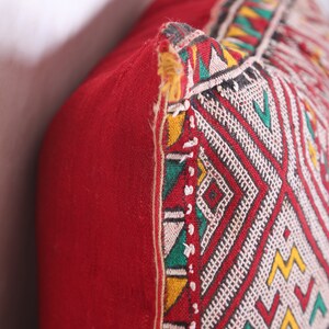 May include: Red throw pillow with a geometric pattern in white, yellow, green, and black. The pillow has a fringe trim.